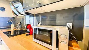 Een keuken met een magnetron, een rode waterkoker en een klok aan de muur.