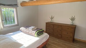 Ein Schlafzimmer mit Bett, Holzboden, Kommode und Fenster mit Blick auf Bäume.