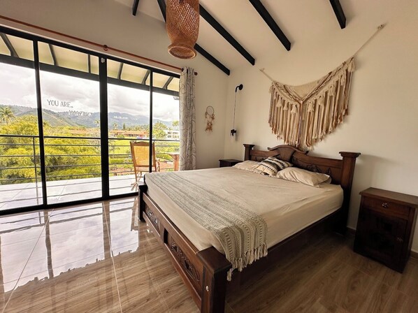 A bedroom with a large window, a bed, a nightstand, and a hanging chair.