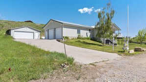 Une maison de plain-pied avec un garage, une véranda et un petit abri de jardin séparé.