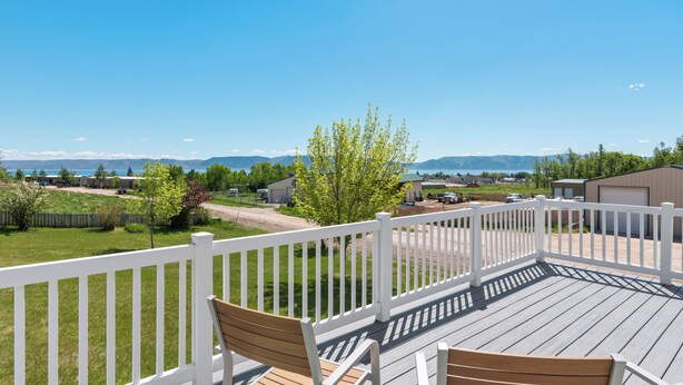 Une terrasse dotée de chaises en bois et d’une balustrade blanche, qui offre une vue sur un quartier résidentiel avec ses maisons et un ciel bleu dégagé.