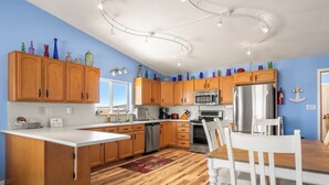 Une cuisine avec des meubles en bois, un plan de travail blanc, des appareils en acier inoxydable et un coin repas avec une table et des chaises blanches.