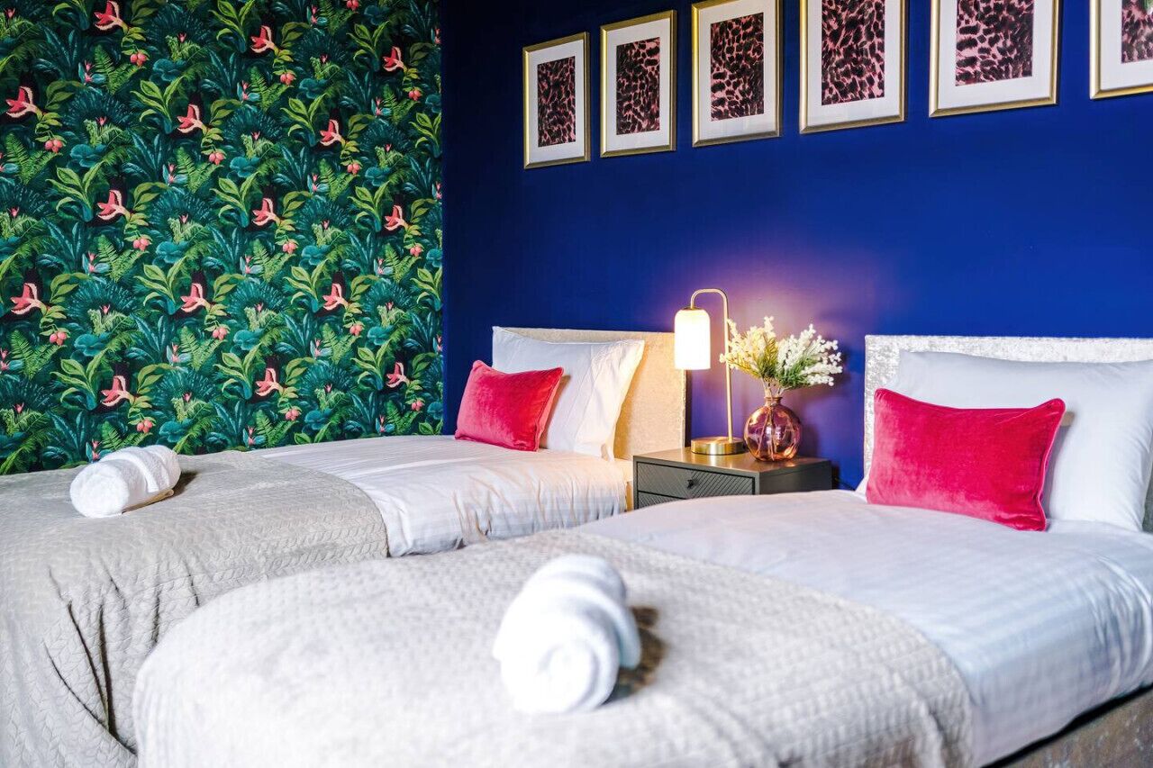 Una habitación de hotel con dos camas, una mesita de noche con lámpara y una pared decorada con cuadros.