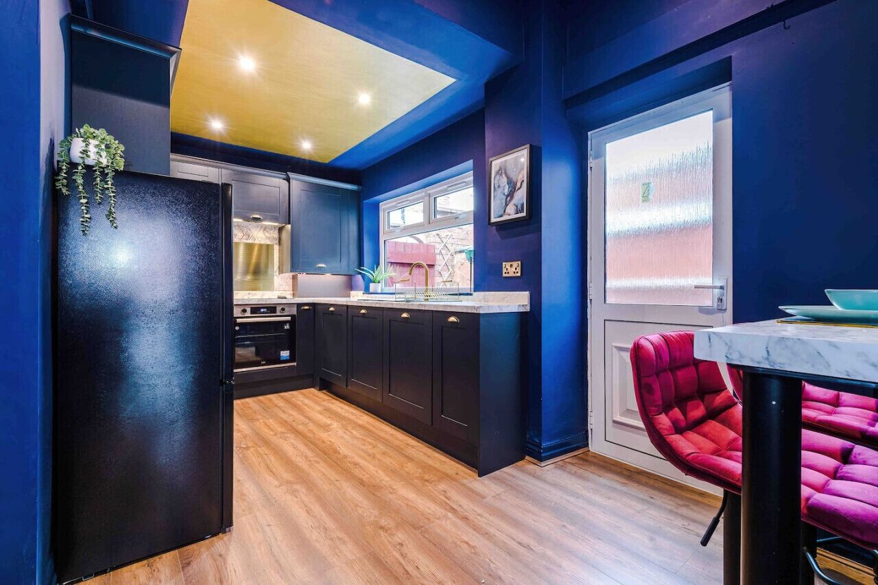 Une cuisine moderne avec des meubles de couleur sombre, un plancher en bois et une chaise rouge.