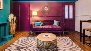 A room with a purple velvet sofa, a round coffee table, and a wall-mounted lamp. - Large 5 Bedroom Home perfect for groups (Salford)