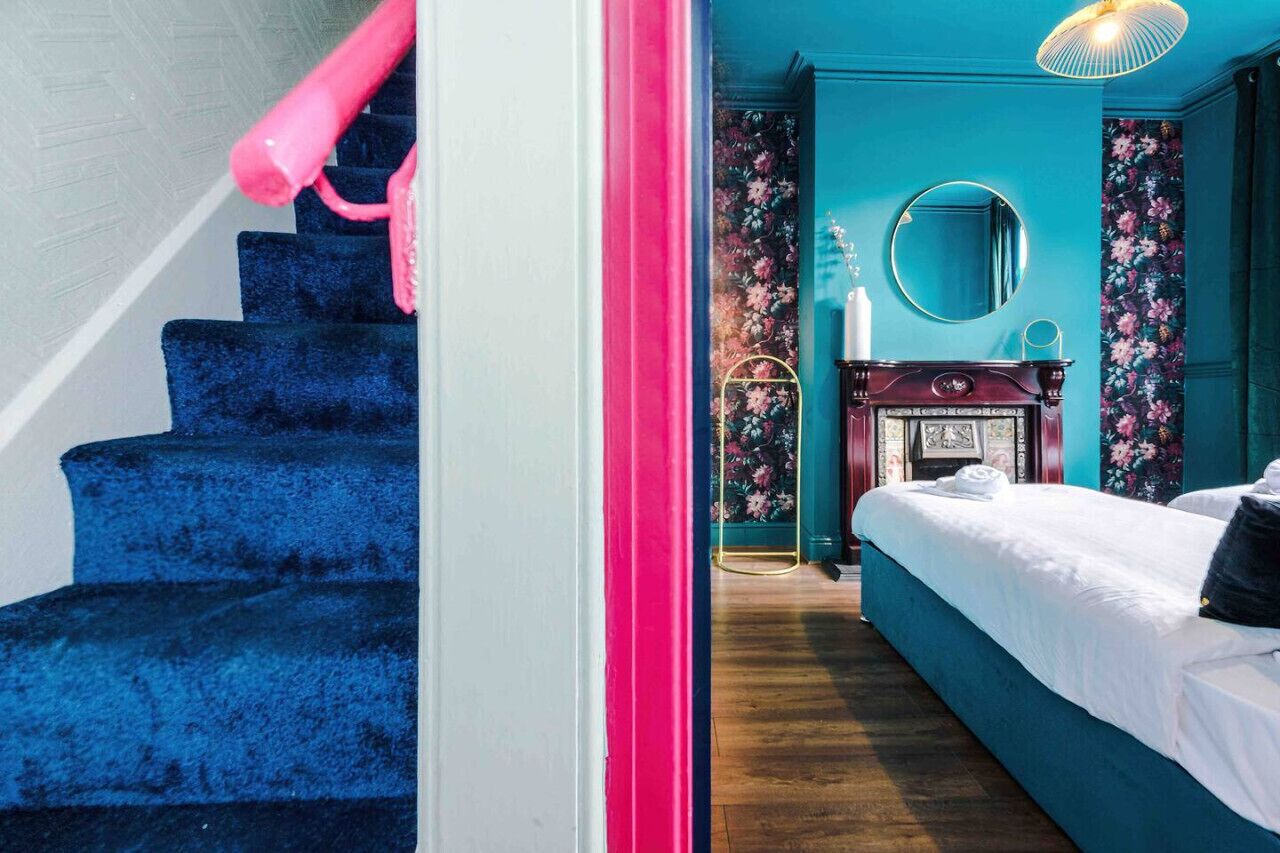 A bedroom with a bed, a dresser, a mirror, and a fireplace.