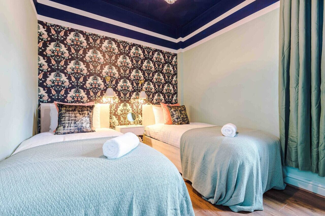 A hotel room with two beds, a patterned wallpaper, and a chandelier.