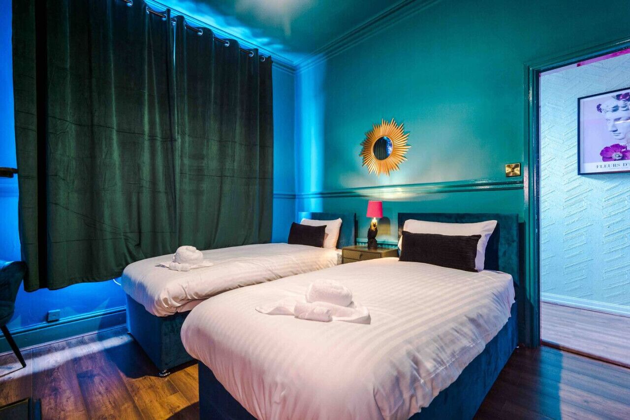 A hotel room with two beds, a nightstand with a lamp, a wall-mounted mirror, and a framed picture on the wall.
