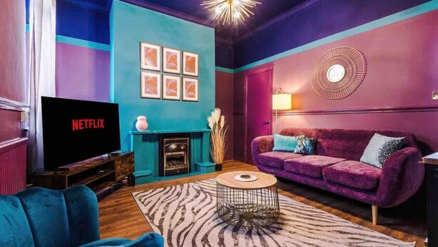 A modern living room with a teal accent wall, a purple sofa, a flat-screen TV, and a fireplace. - Large 5 Bedroom Home perfect for groups (Salford)
