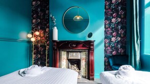 A room with teal walls, a fireplace, two beds, and a floral-patterned curtain. - Large 5 Bedroom Home perfect for groups (Salford)