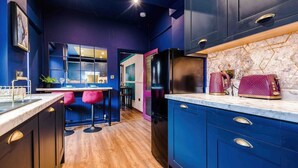 A modern kitchen with dark blue cabinets, a marble countertop, and a black refrigerator. There is a bar area with stools and a large window. - Large 5 Bedroom Home perfect for groups (Salford)