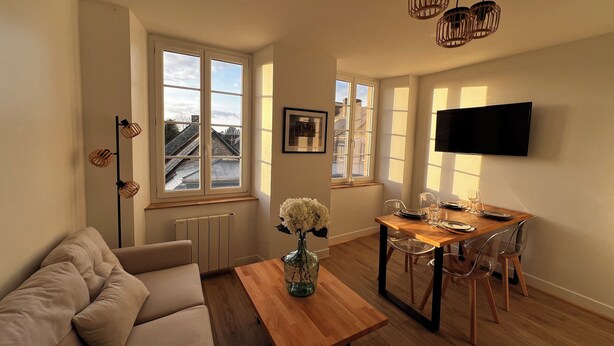 A modern living room with a sofa, a wooden coffee table, and a dining area with a TV and table set.