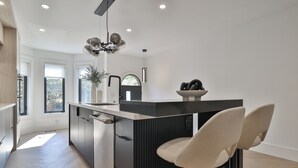 Eine moderne Küche mit einer zentralen Kochinsel, Barhocker und einer Pendelleuchte.