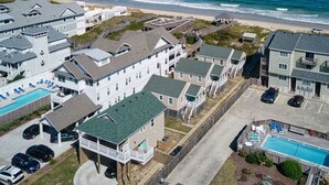 A coastal residential area with houses, a swimming pool, and a beach in the background.