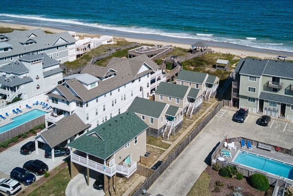 A coastal residential area with houses, a swimming pool, and a beach in the background.
