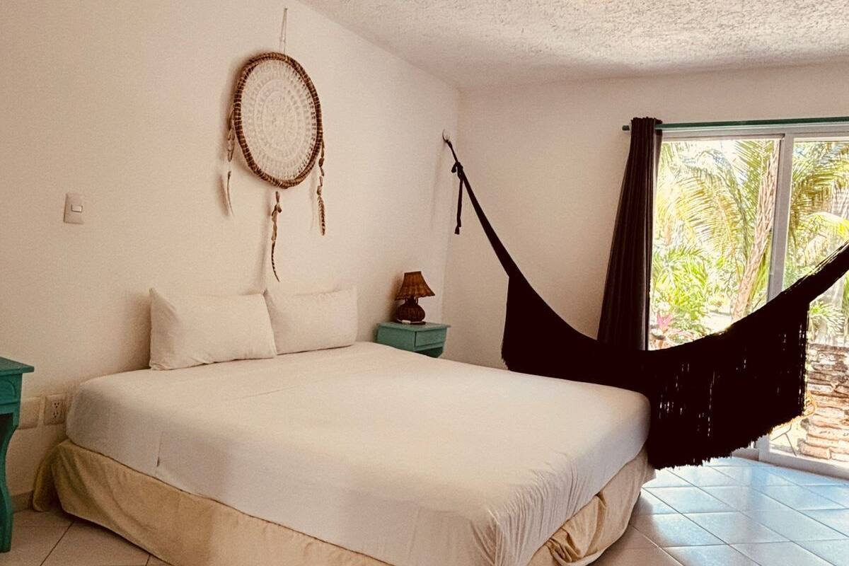 A bedroom with a bed, a hanging chair, a wall hanging, and a window with curtains.