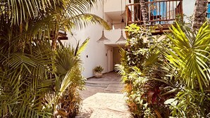Un estrecho sendero de piedra bordeado de exuberante vegetación tropical que conduce a un edificio con balcón.