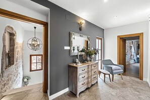 A hallway with a stone wall, a wooden door frame, a dresser with drawers, a chair, and a mirror on the wall. - Castle with Stunning Views by Aneo Travel (Bribir)