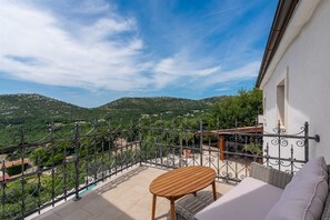 Un balcón con mesa de madera y cojines blancos, con vista a un paisaje montañoso.