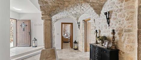 A hallway with stone walls, a wooden door, a black dresser, and a tiled floor.