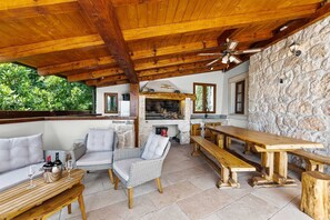 An outdoor patio with wooden furniture, a stone wall, and a stone fireplace.