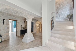 A stone-walled interior with a central column, a staircase, and a kitchen area.