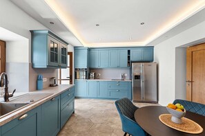 A modern kitchen with teal cabinets, stainless steel appliances, and a dining area with a blue chair and table. - Castle with Stunning Views by Aneo Travel (Bribir)