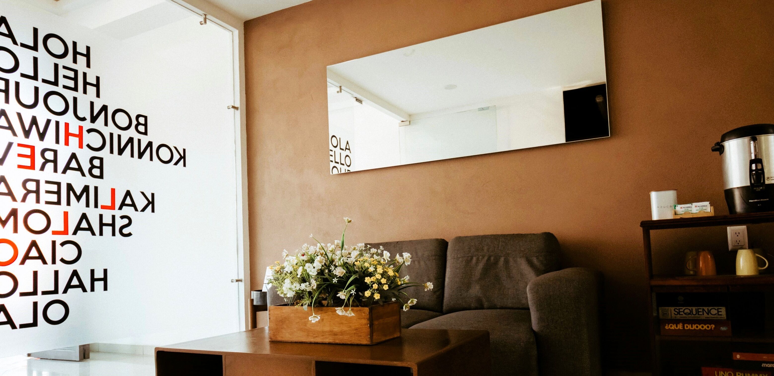 Ein modernes Wohnzimmer mit einer Couch, einem Couchtisch mit Blumen, einem Bücherregal und einem großen Spiegel an der Wand.