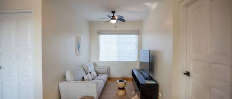 Un salon avec un canapé, une table basse, un téléviseur et un ventilateur de plafond.