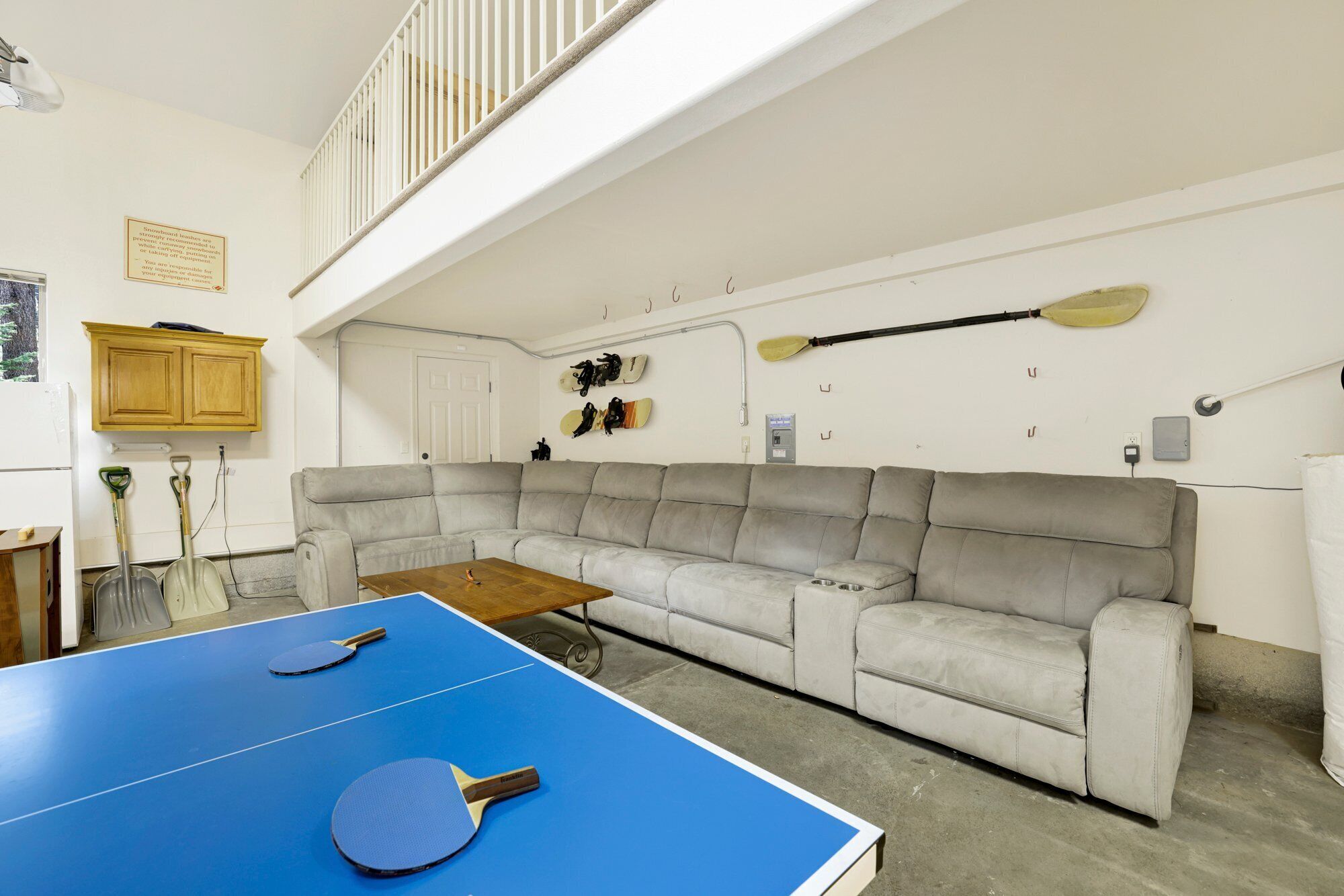 A room with a blue ping pong table, a grey sofa, and paddleboards on the wall.