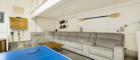 A room with a blue ping pong table, a grey sofa, and paddleboards on the wall.