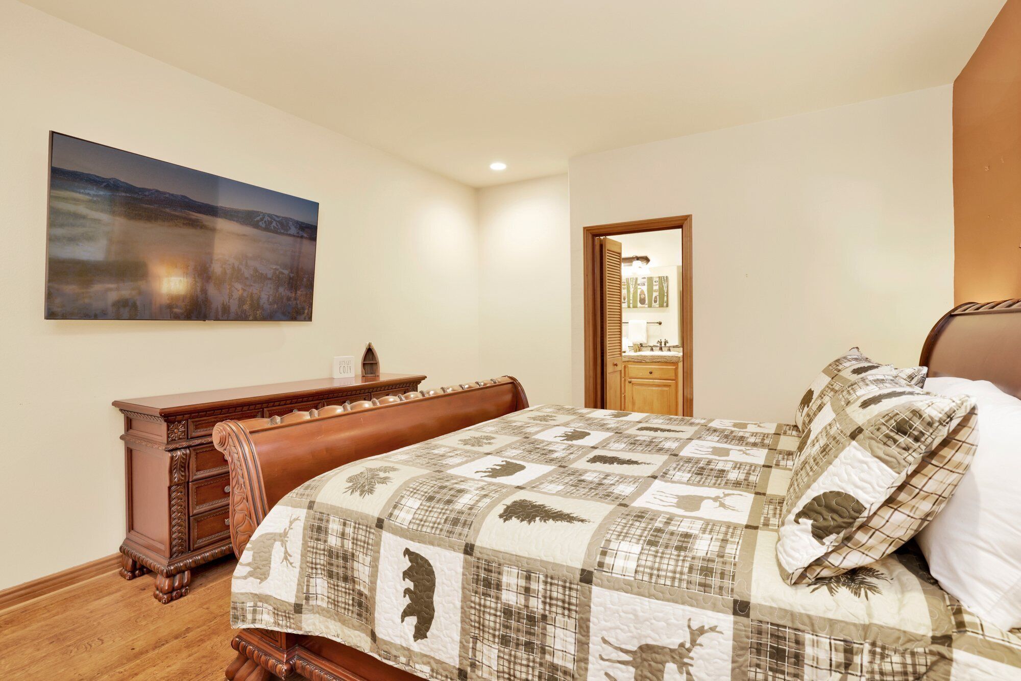 A bedroom with a large bed, a wooden dresser, a painting on the wall, and a door leading to a bathroom.