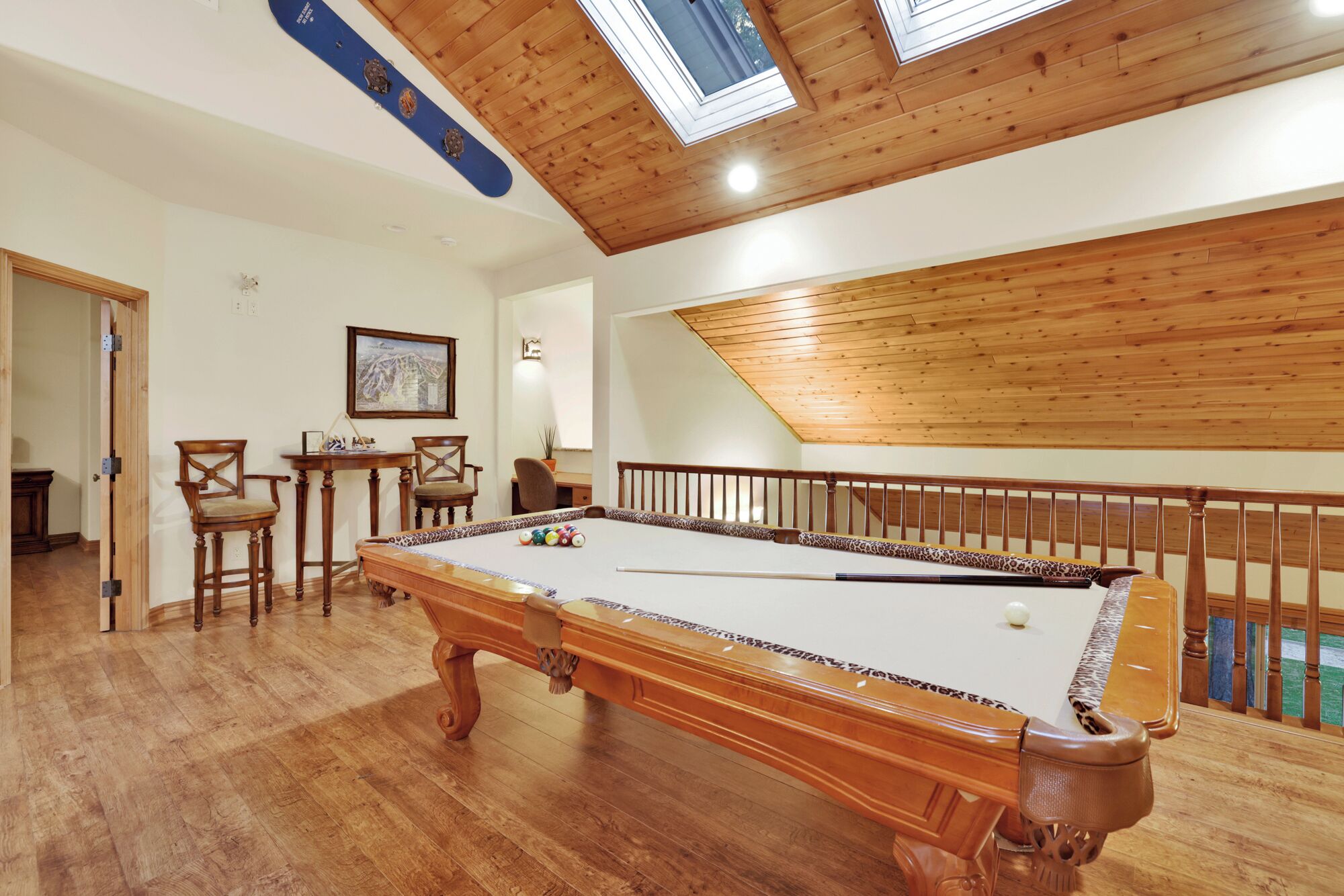 Une table de billard dans une pièce dotée d’un plancher en bois, d’un plafond en bois et offrant une vue sur le ciel grâce à une lucarne.