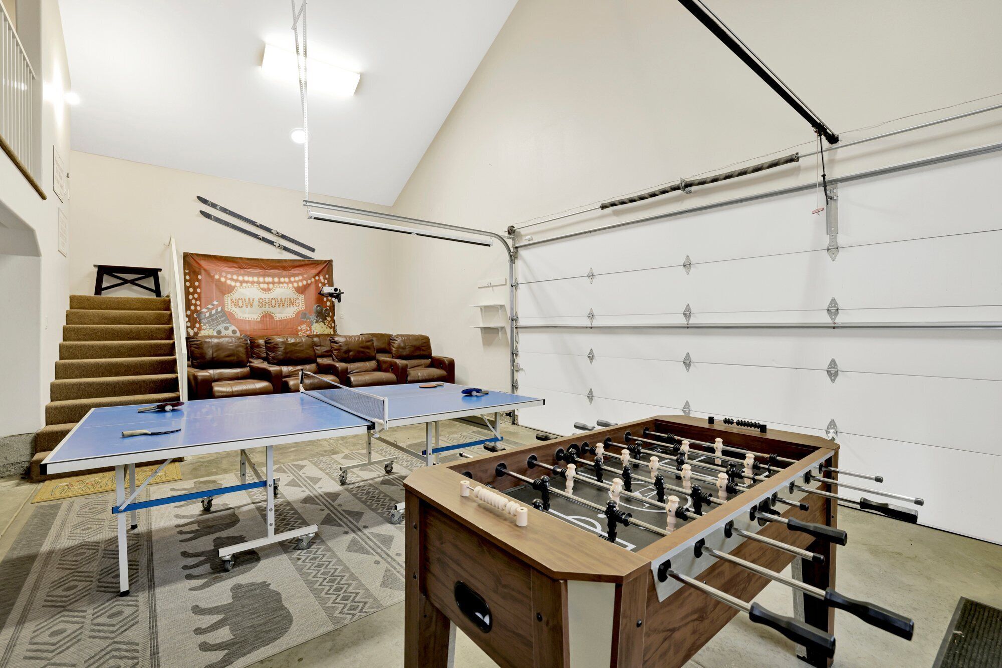 A room with a ping pong table, a foosball table, a sofa, and a staircase.
