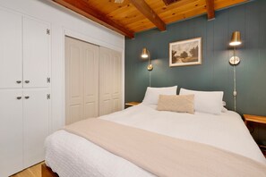 Un dormitorio con una cama grande, dos lámparas de noche, un cuadro enmarcado en la pared y un armario blanco con varias puertas.