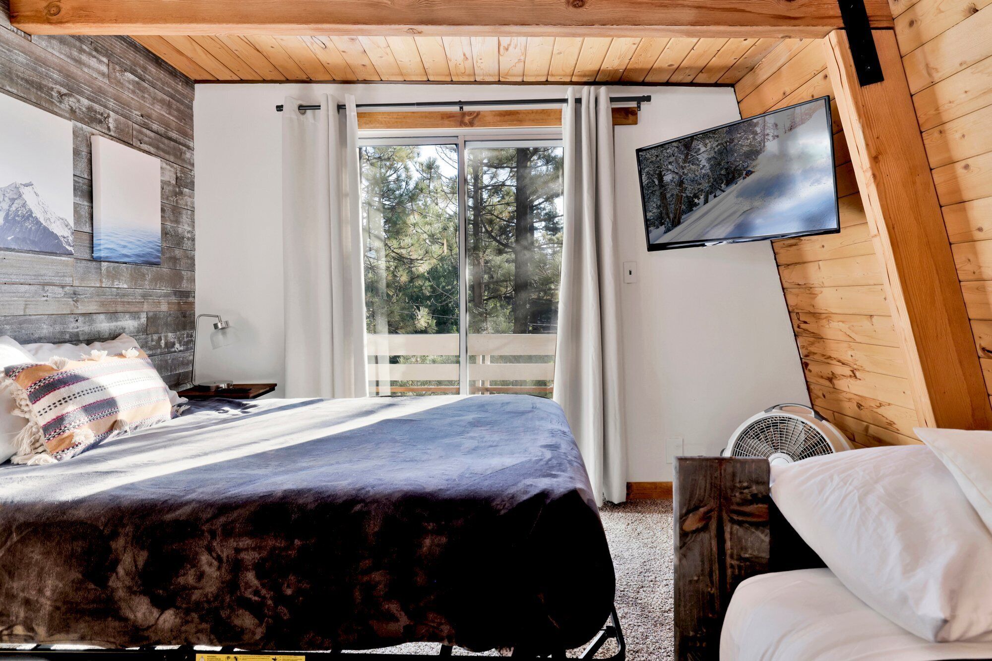 Une chambre à coucher avec un lit, une télévision, une fenêtre avec des rideaux et une vue sur les arbres.