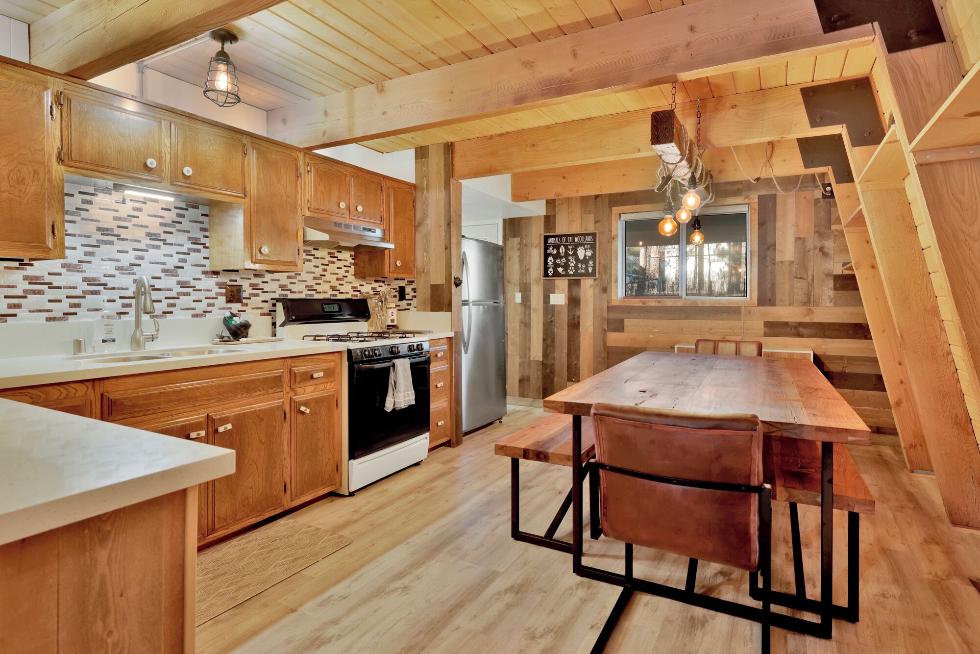 A modern kitchen with wooden cabinets, a tiled backsplash, and a large island with a sink. There is a stove, refrigerator, and a sign on the wall.