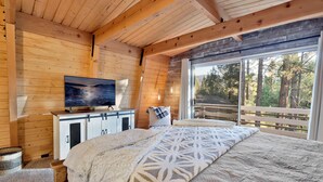Une chambre à coucher située dans une cabane en bois, avec un grand lit, un téléviseur posé sur une commode et une vue sur les arbres par une grande fenêtre.