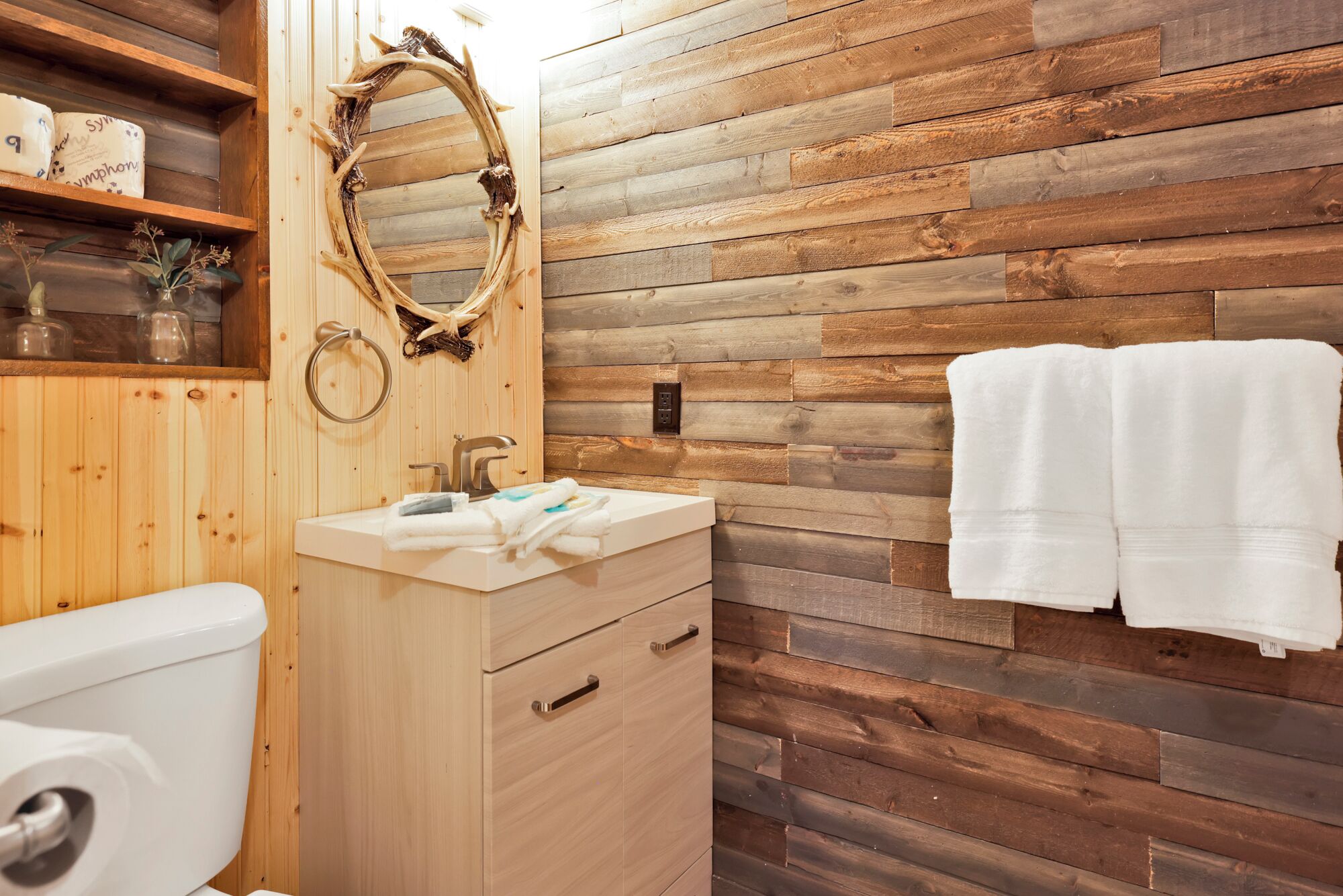 A bathroom with a wooden wall, a sink with a mirror, and a toilet.