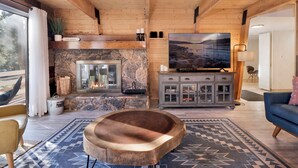 Un salon chaleureux avec une cheminée en pierre, un grand téléviseur à écran plat, une table basse en bois et un canapé bleu.
