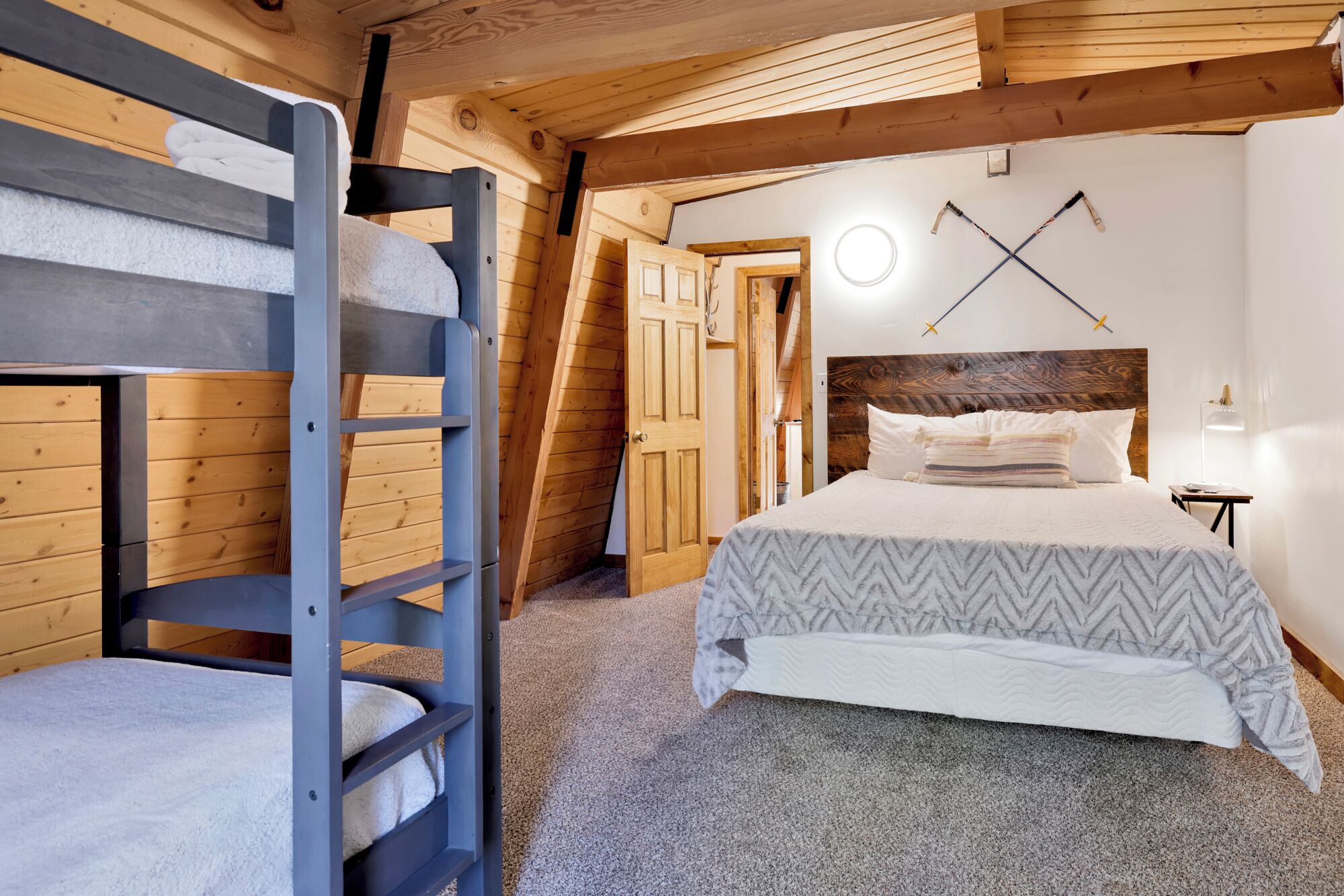A cozy bedroom with a bunk bed, a wooden ceiling, and a bed with a headboard.