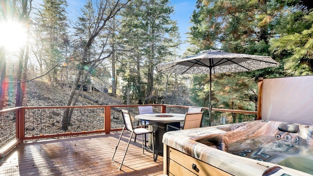 A wooden deck with a hot tub, a table, and chairs, surrounded by trees. - Silvertip Pines #2335 (Big Bear Lake)