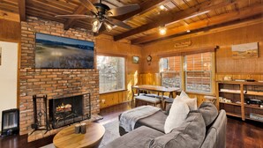 A cozy cabin interior with a fireplace, wooden ceiling, and a large window overlooking a snowy landscape. - Silvertip Pines #2335 (Big Bear Lake)