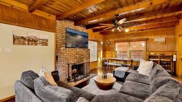 A cozy living room with a fireplace, a large sofa, and a dining area with a table and chairs.