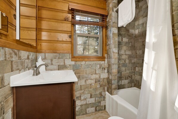 Une salle de bain avec un mur en pierre, un meuble-lavabo en bois, une fenêtre et une baignoire.