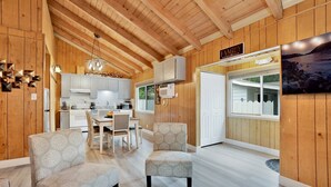 A cozy cabin interior with a dining area, kitchen, and a large window offering a scenic view.