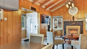 A cozy cabin interior with a dining area, a fireplace, and a large clock on the wall.