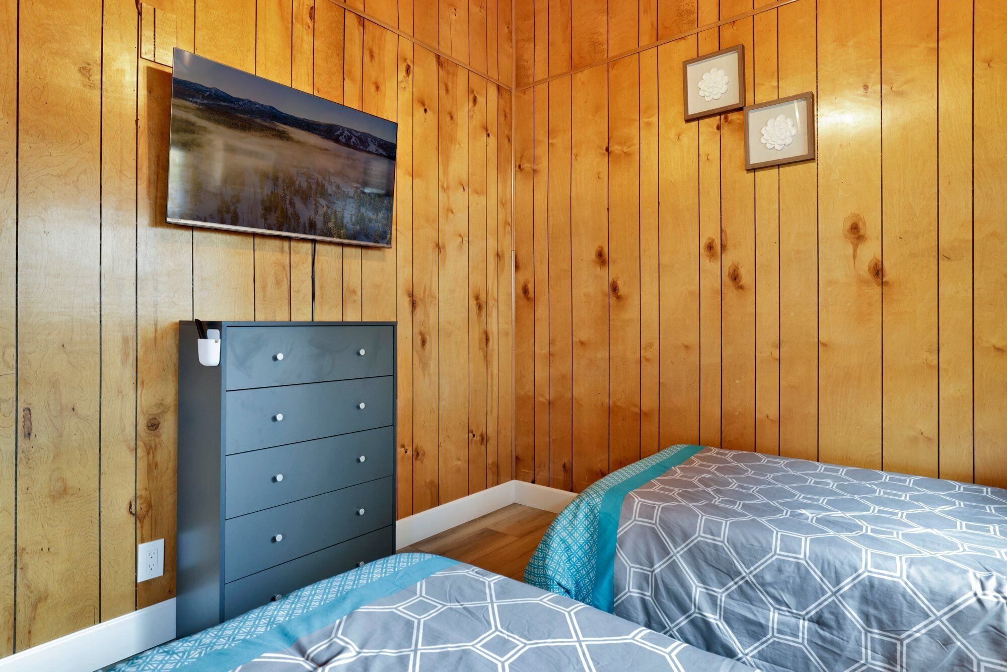 A wooden-paneled room with a bed, a dresser, and a framed picture on the wall.