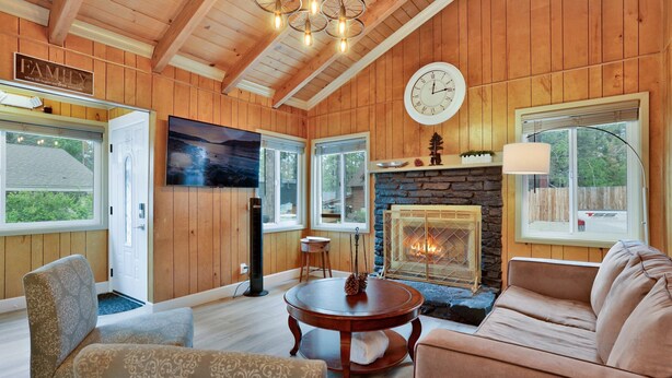 A cozy living room with wooden walls, a stone fireplace, a large clock, and a television.