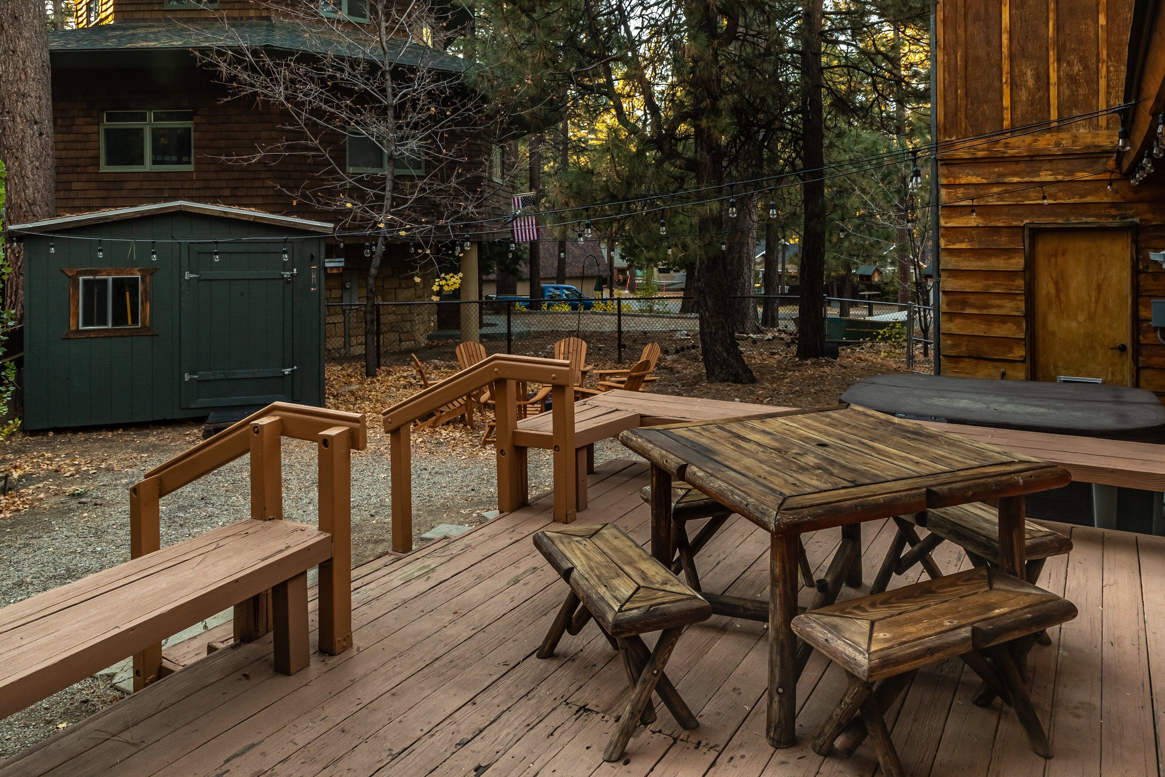 A wooden deck with picnic tables and benches, surrounded by trees and a cabin.